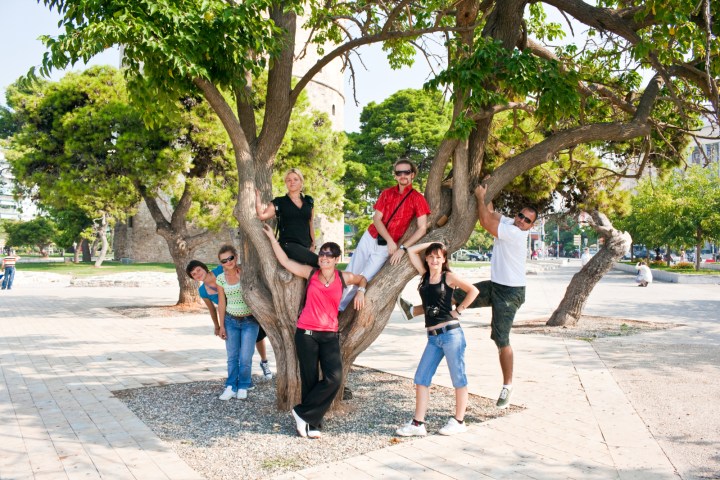 a group of people walking down a sidewalk next to a tree